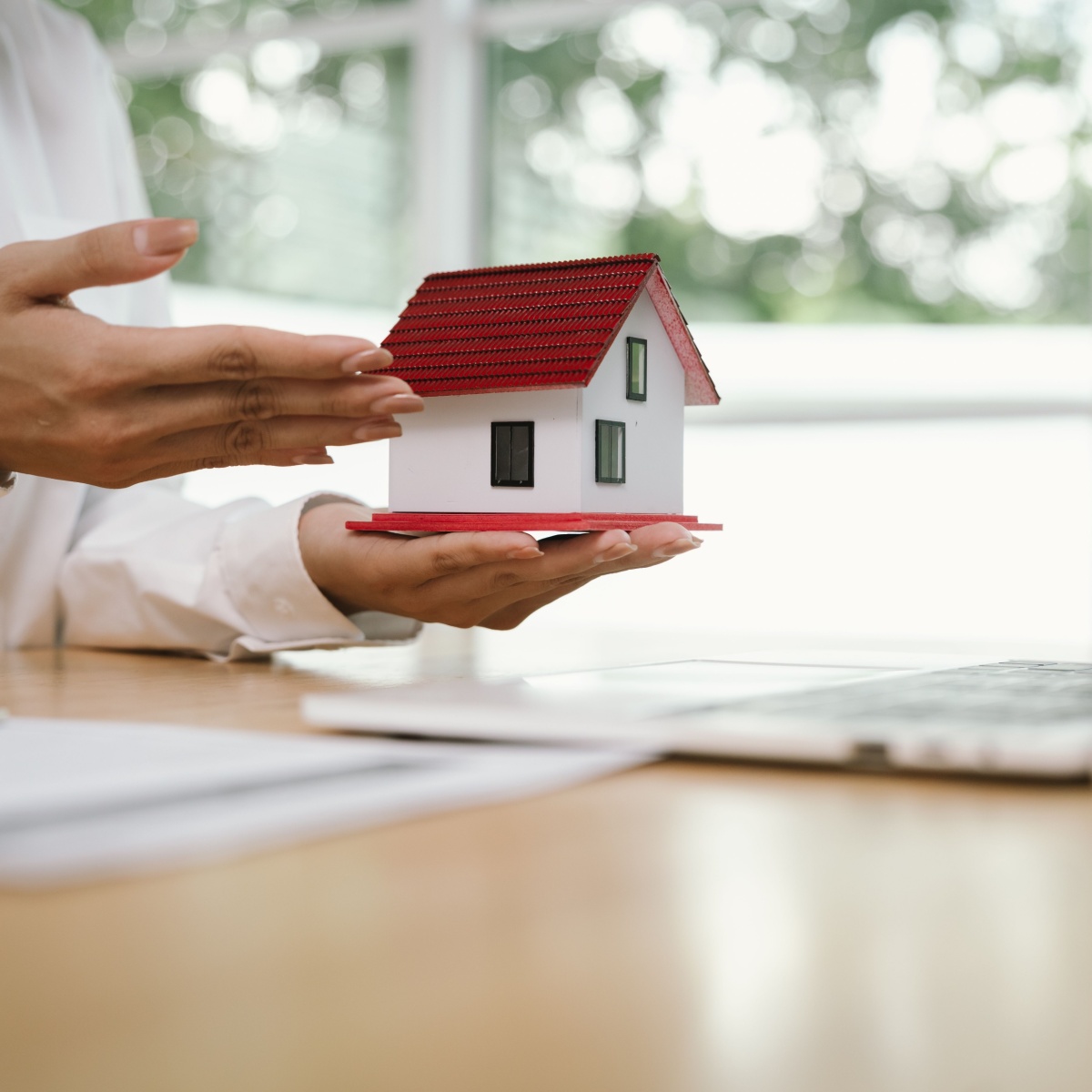 Manos sosteniendo una maqueta de vivienda junto a un portátil: cancelación de hipoteca y plazos en la compraventa