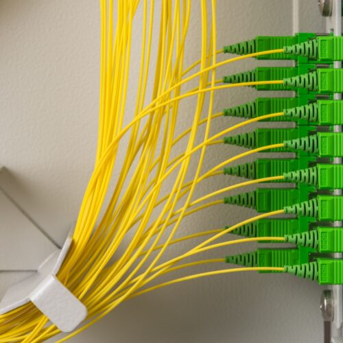 Cables de fibra óptica amarillos conectados a un panel de distribución con conectores verdes SC/APC en una central de telecomunicaciones para comunicaciones gigabit en cumplimiento con la Ley Europea de Infraestructura de Gigabit
