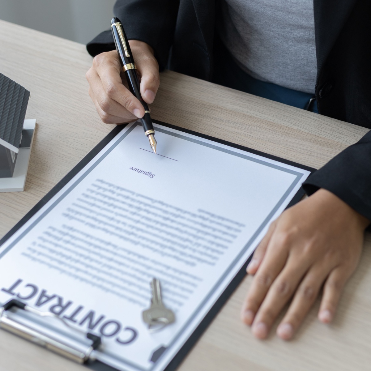 Firma de contrato de compraventa con llaves y maqueta de vivienda
