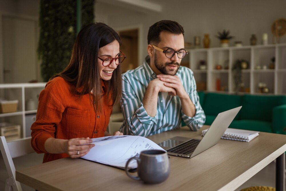 Couple reviewing documents and family financial resources together at a laptop