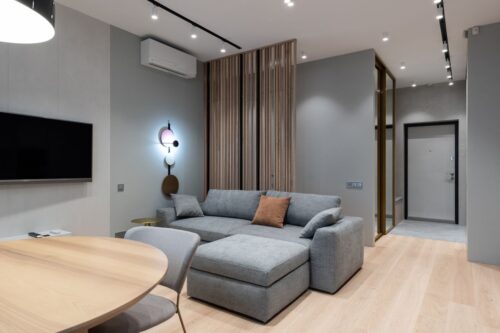 Salón de una vivienda amueblada con sofá gris y mesa de madera